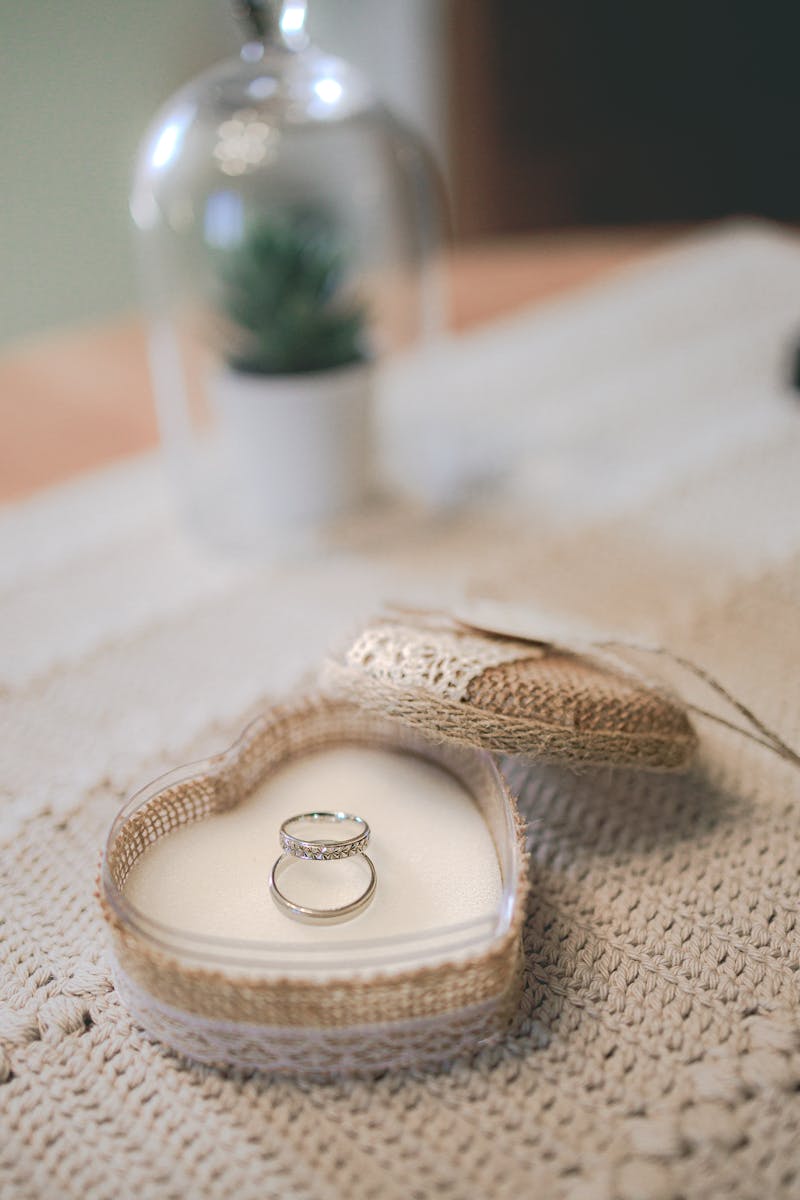 Close-up of wedding rings in a crochet heart box on a table.